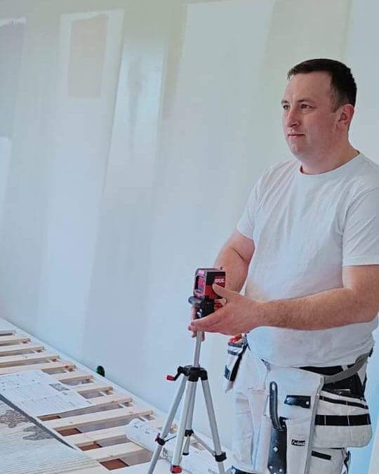 Kamil Winiarski i arbetskläder ställer in ett laserlod inför en tapetsering