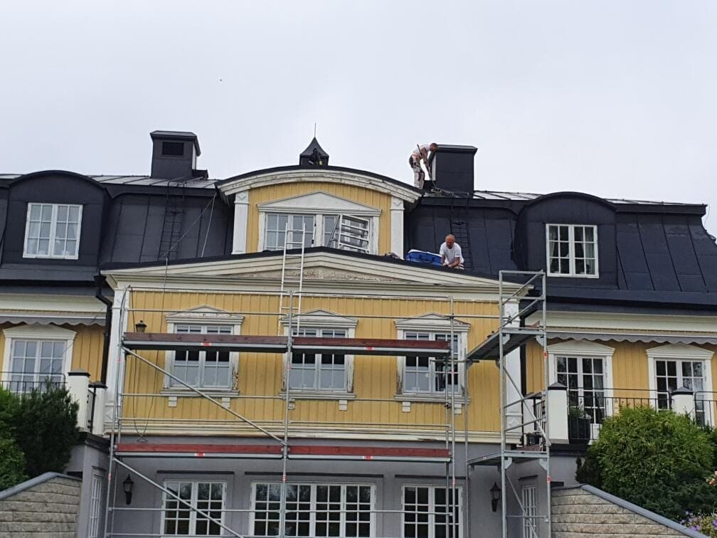 Målare på taket till en gul villa med brutet tak