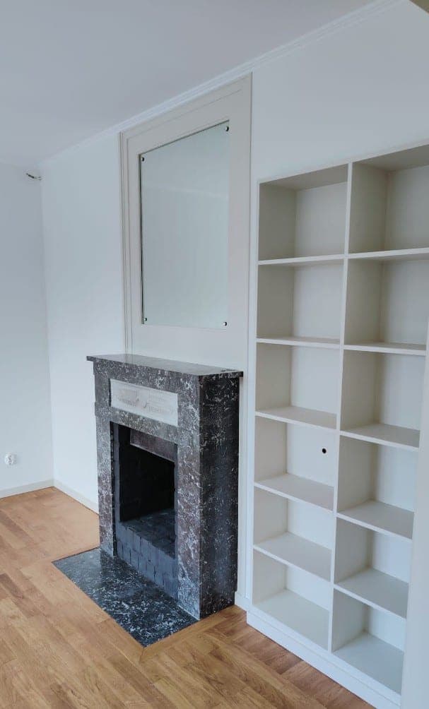 Vitmålad vägg och bokhylla bredvid en öppen spis